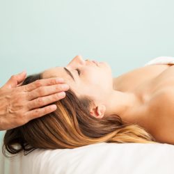 Profile view of a cute young woman getting her energy balanced at a reiki session in a health clinic and spa